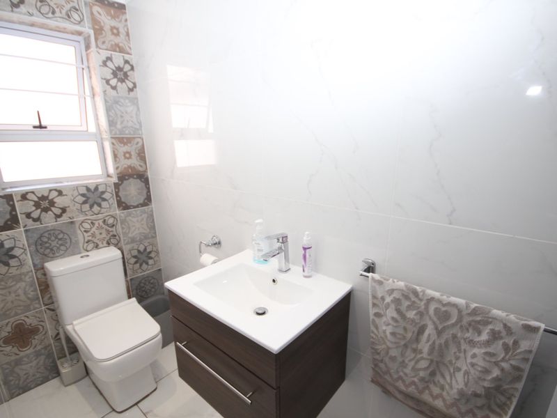 A modern bathroom featuring a wall-mounted vanity with basin, a sleek toilet, and decorative patterned wall tiles surrounding the window.