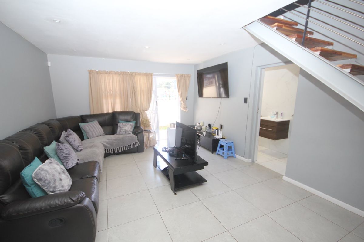 Spacious living room featuring neutral tiled flooring, recessed lighting, and a modern staircase, with direct access to an outdoor area through sliding glass doors.