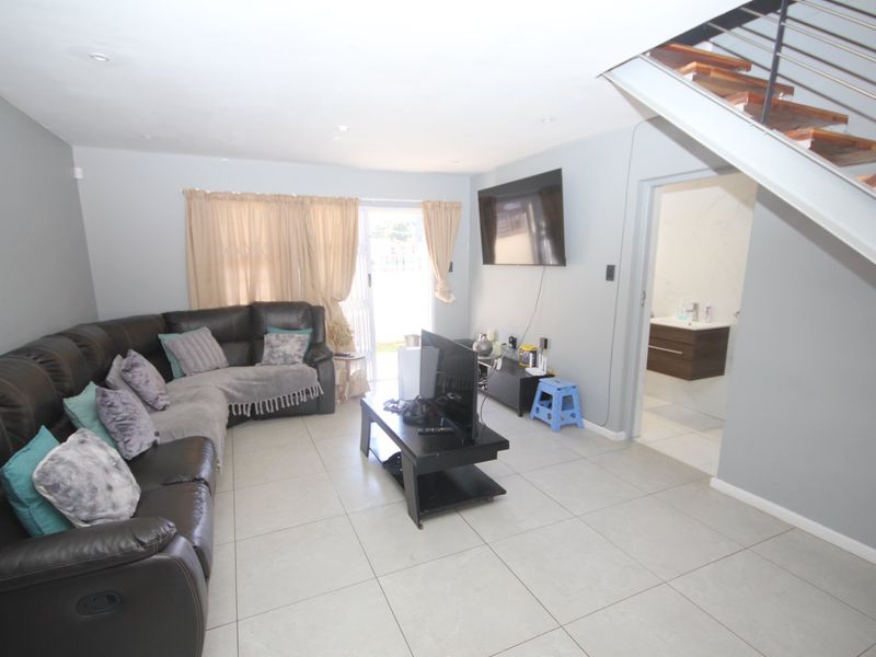 Spacious living room featuring neutral tiled flooring, recessed lighting, and a modern staircase, with direct access to an outdoor area through sliding glass doors.