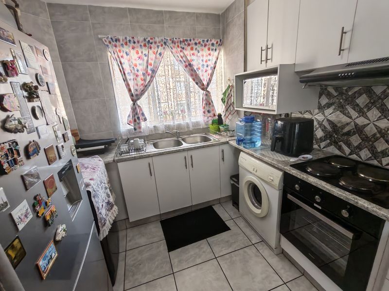 Compact kitchen featuring built-in cabinetry, a double sink, electric hob, oven, extractor fan, and tiled finishes throughout.