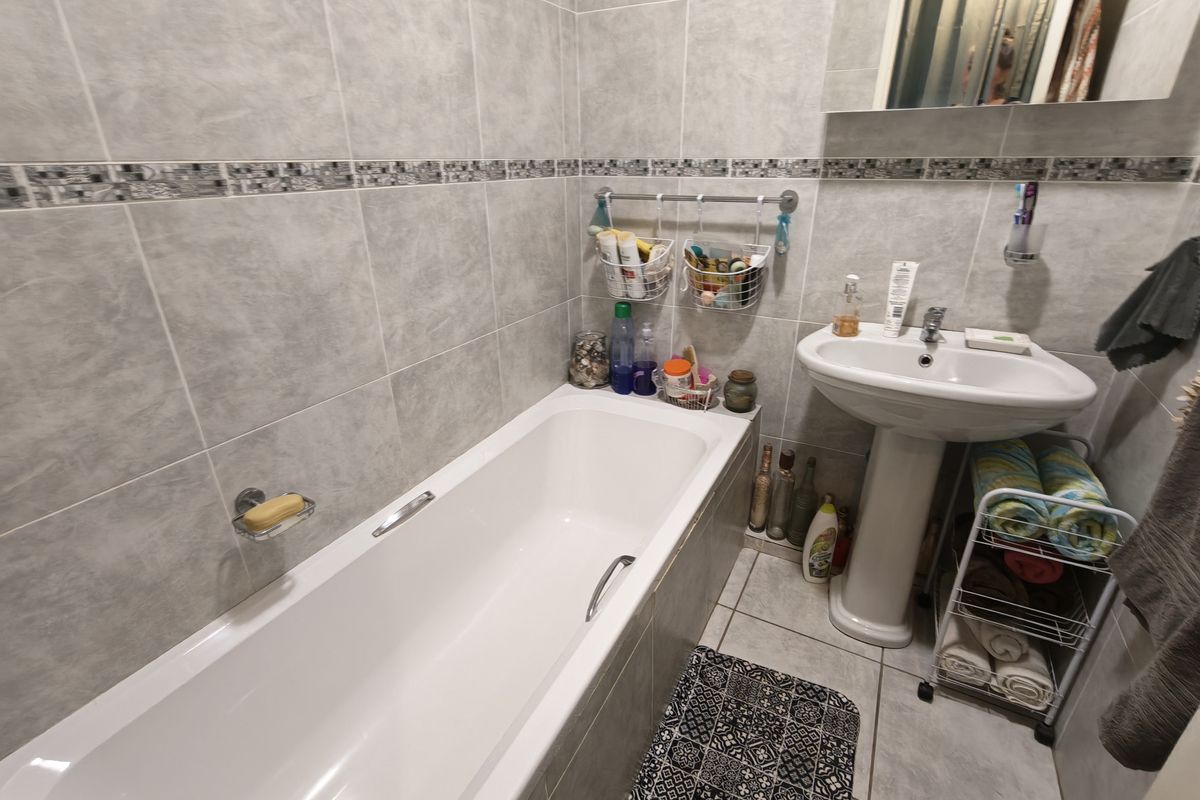 A functional bathroom featuring a pedestal basin, a standard bathtub, and full-height wall tiling with a decorative border.