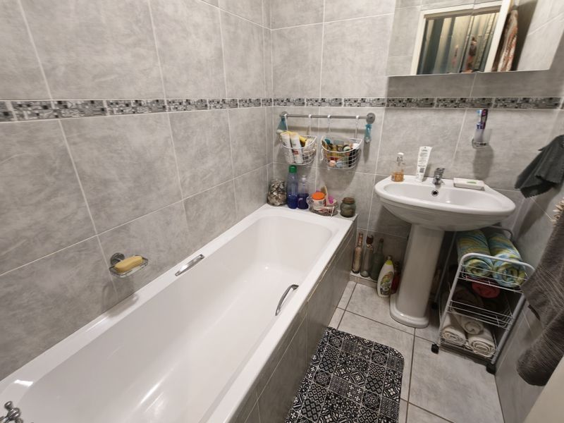 A functional bathroom featuring a pedestal basin, a standard bathtub, and full-height wall tiling with a decorative border.
