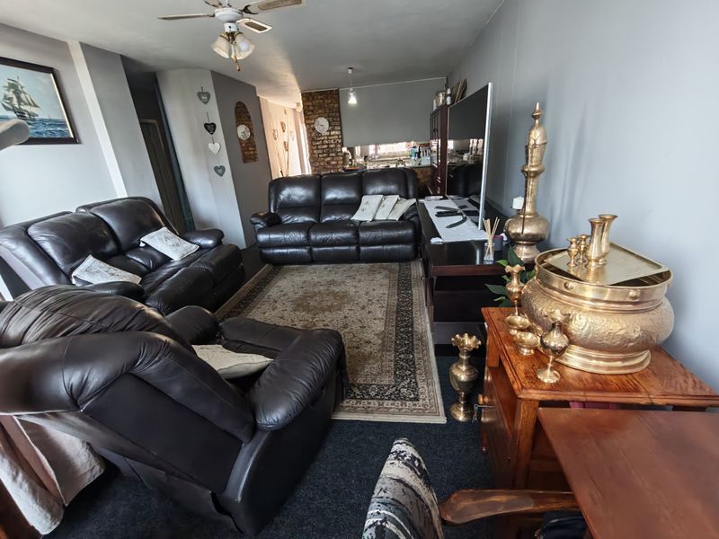Open plan living area featuring a ceiling fan and an exposed brick wall, connecting to the kitchen space.