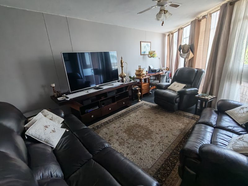 A spacious living room featuring a ceiling fan and large windows with natural light, offering a comfortable area for relaxation.