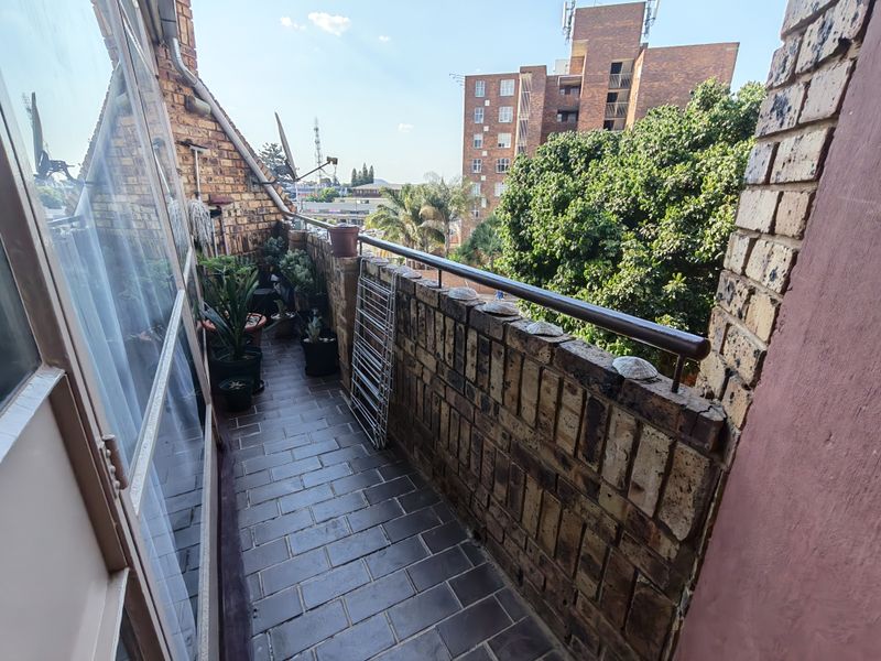 A narrow balcony featuring brick walls, a metal handrail, and tiled flooring, offering an elevated view of the surrounding urban area.
