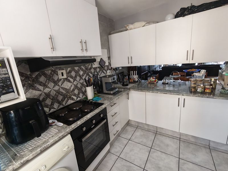 A functional kitchen featuring white cabinetry, granite-look laminate countertops, a built-in oven with electric hob, and tiled flooring throughout.