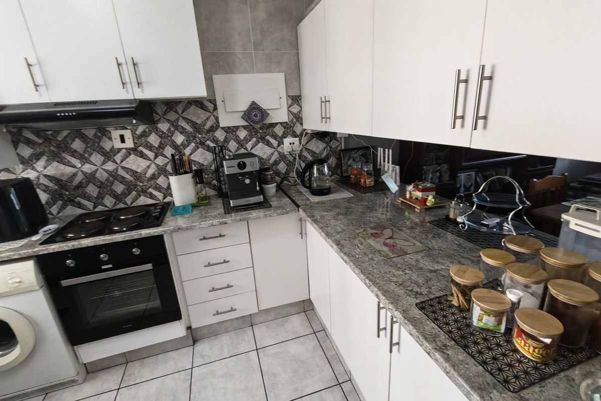 A functional kitchen featuring white cabinetry, granite countertops, a built-in oven, hob, and extractor fan with a decorative tiled backsplash.