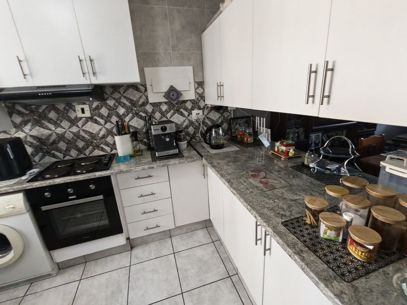 A functional kitchen featuring white cabinetry, granite countertops, a built-in oven, hob, and extractor fan with a decorative tiled backsplash.