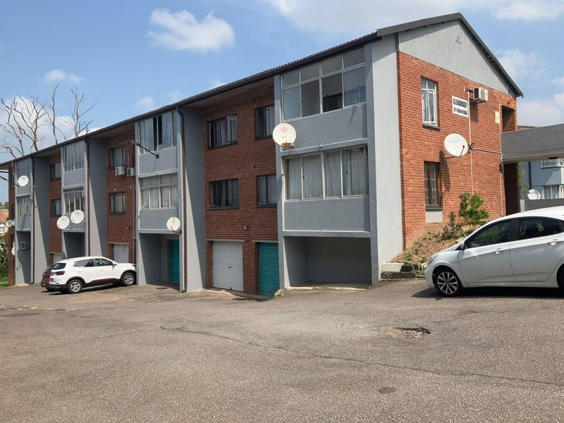 Exterior view of a multi-story townhouse complex featuring brick and painted facade, roller garage doors, and an asphalt driveway.