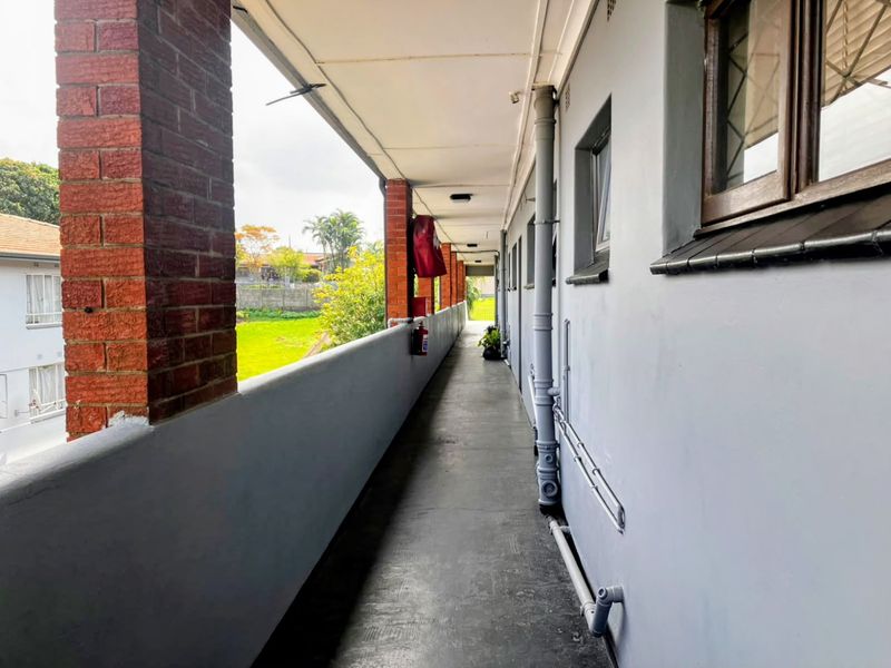 An exterior open-air walkway featuring brick pillars and concrete flooring, providing access to the townhouse units.