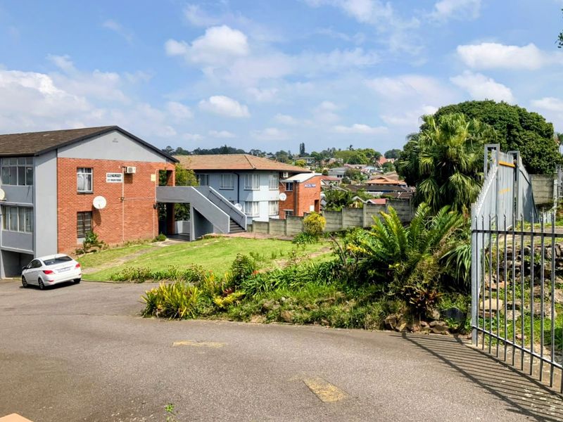 Exterior view of a brick townhouse complex featuring a paved driveway, communal garden area, and external concrete staircase access.