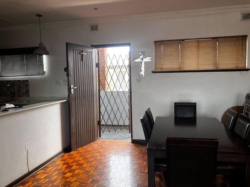 Open plan living and dining area featuring classic parquet flooring, natural light through venetian blinds, and direct access to an exterior security gate.