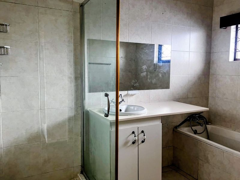 A functional bathroom featuring a vanity cabinet with integrated sink, a bathtub, and a separate shower enclosure with full-height wall tiling.