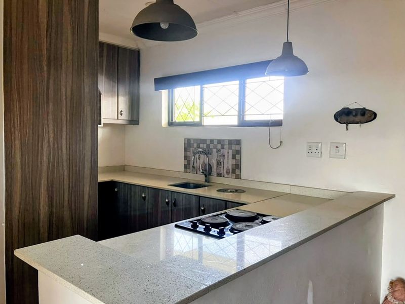 A functional kitchen featuring dark wood-grain cabinetry, stone countertops, a built-in hob, and a tiled splashback with a window for natural light.