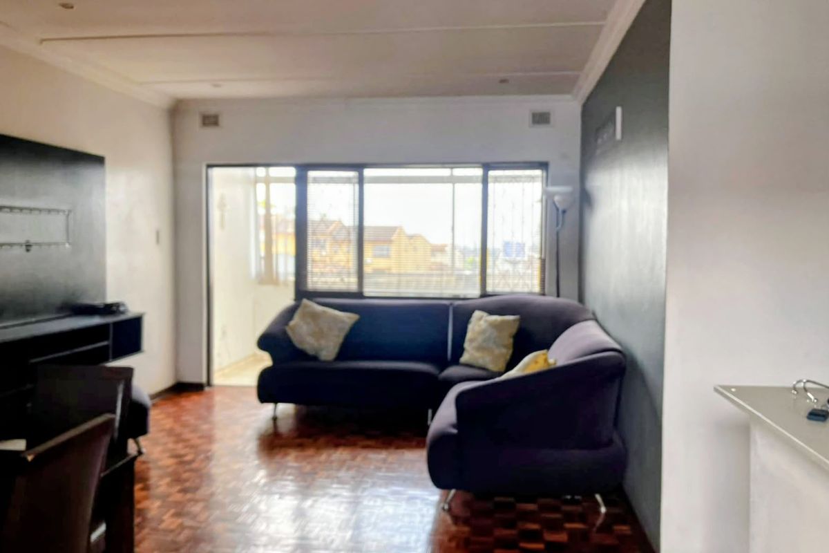 A living room featuring parquet flooring, an accent wall, and a sliding glass door leading to an outdoor area.