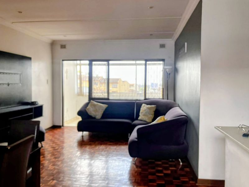 A living room featuring parquet flooring, an accent wall, and a sliding glass door leading to an outdoor area.