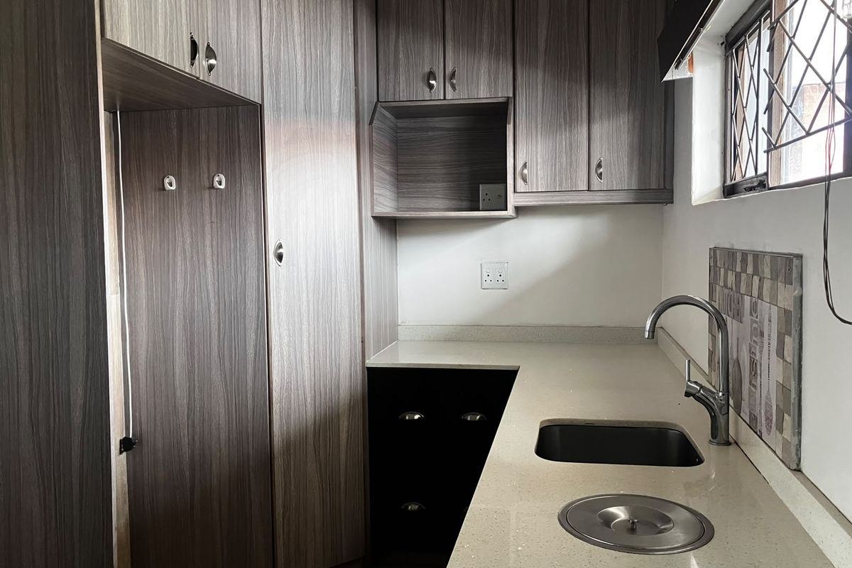 A clean, modern kitchen featuring wood-grain cabinetry, stone countertops, an undermount sink with a mixer tap, and a tiled backsplash.