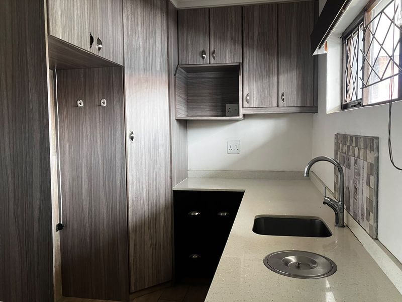 A clean, modern kitchen featuring wood-grain cabinetry, stone countertops, an undermount sink with a mixer tap, and a tiled backsplash.