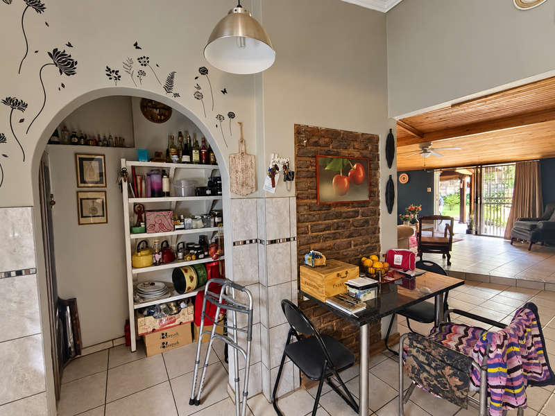 Open plan living area featuring an arched alcove with built-in shelving, an exposed brick feature wall, and tiled flooring leading to an outdoor patio.