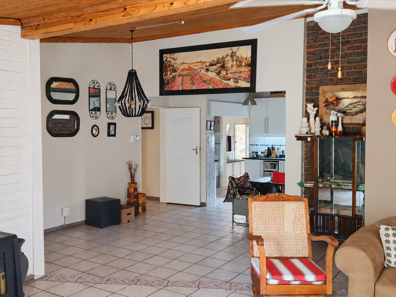 Open plan living area featuring exposed timber ceiling beams, a brick fireplace, and tiled flooring, with a view through to the kitchen area.