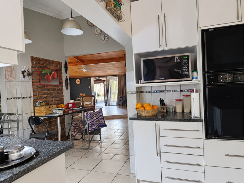 Open-plan kitchen featuring granite countertops, built-in appliances, and an exposed brick feature wall, flowing into a spacious living area with tiled flooring.