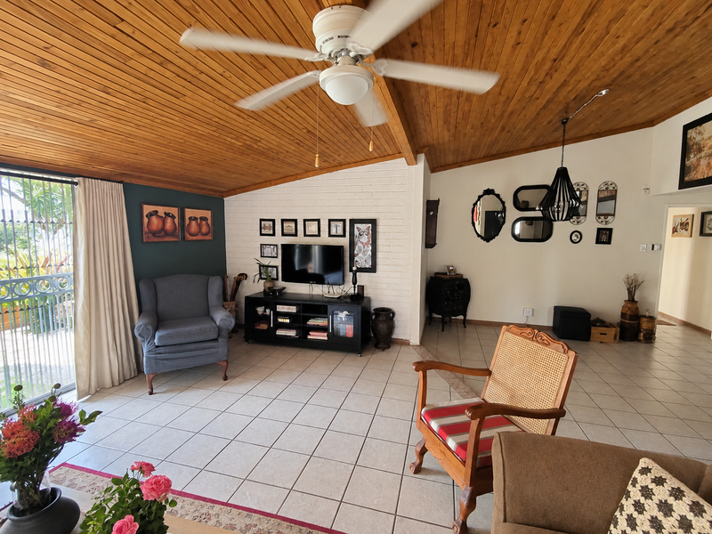 Spacious living room featuring a vaulted timber-clad ceiling, ceramic tiled flooring, and a painted brick feature wall with access to an outdoor patio area.