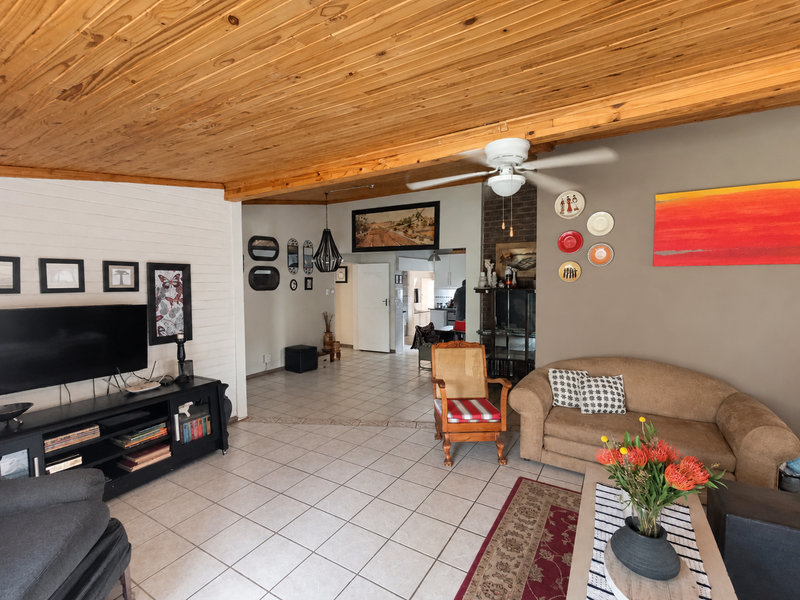 Spacious living room featuring a warm timber-clad ceiling, ceramic floor tiles, and a brick fireplace, creating a cozy and inviting atmosphere.