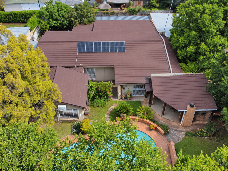 Aerial view of a residential property featuring a tiled roof with solar panels, a swimming pool, and a brick-paved patio area.