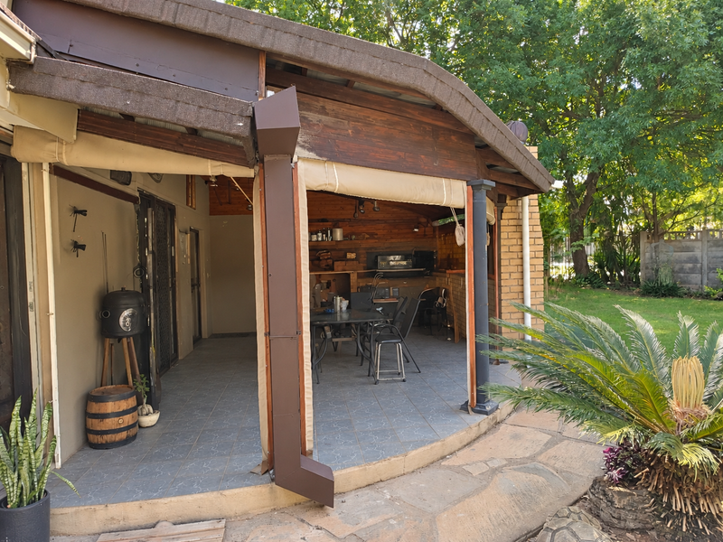 Covered patio area featuring a built-in braai, timber ceiling, and tiled flooring, providing a functional outdoor entertainment space overlooking the garden.