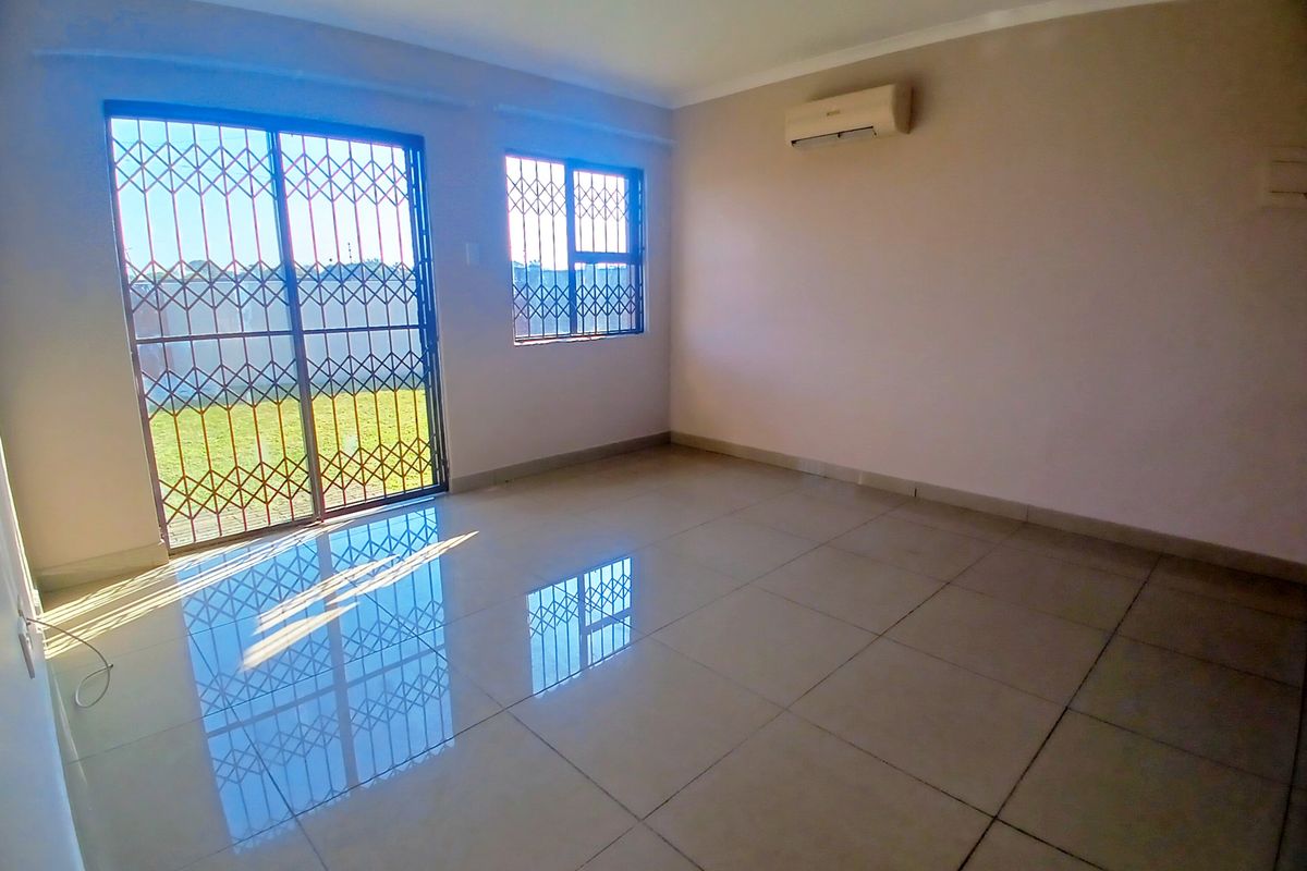 A bright, empty living room featuring large format floor tiles, an air conditioning unit, and sliding doors leading to an outdoor area.