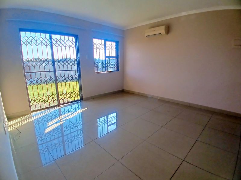 A bright, empty living room featuring large format floor tiles, an air conditioning unit, and sliding doors leading to an outdoor area.