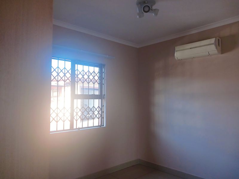 An empty bedroom featuring a wall-mounted air conditioning unit, a window with a security gate, and a ceiling light fixture.