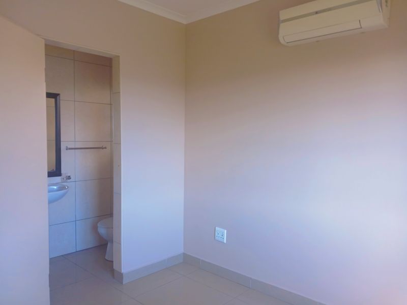 A clean, empty bedroom featuring tiled flooring, a wall-mounted air conditioning unit, and an adjoining en-suite bathroom.