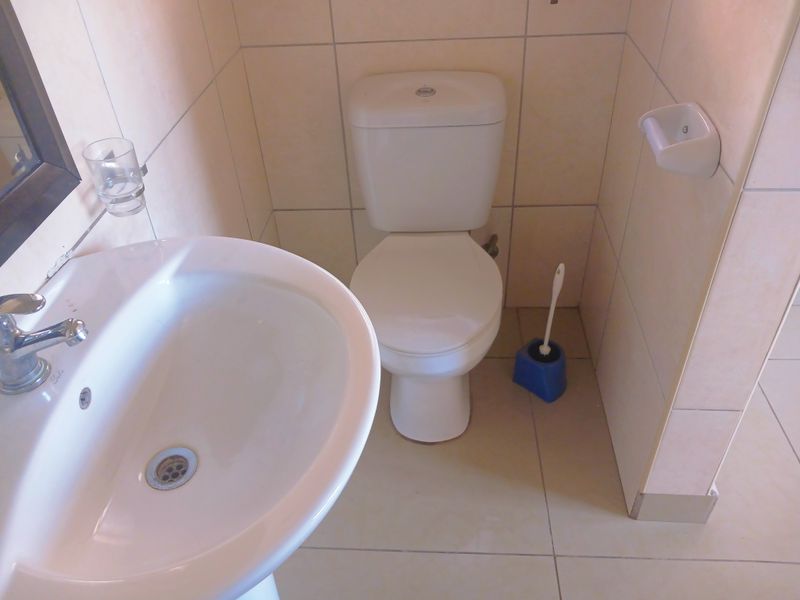 A compact bathroom featuring a white pedestal basin and toilet with neutral ceramic wall and floor tiling.