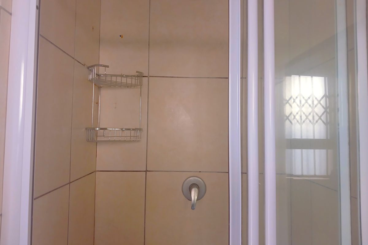 A functional shower enclosure featuring tiled walls, a standard shower mixer, and a security gate on the adjacent window.