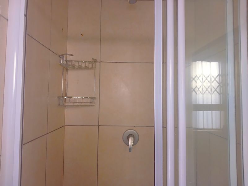 A functional shower enclosure featuring tiled walls, a standard shower mixer, and a security gate on the adjacent window.