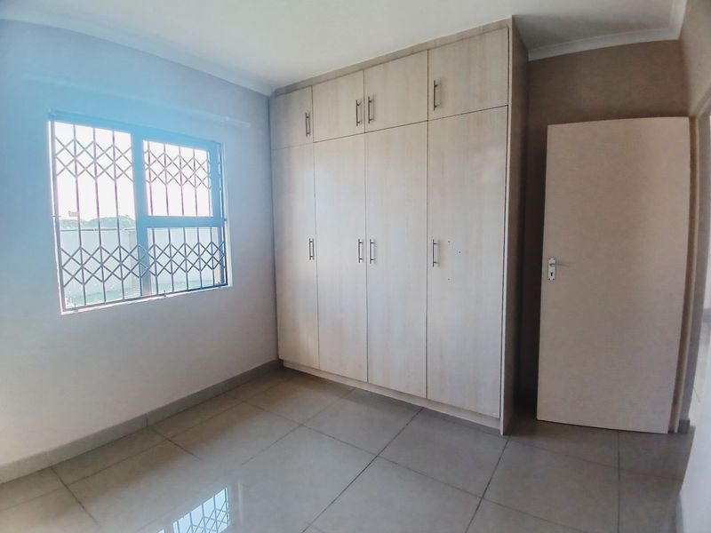 A bright, empty bedroom featuring neutral tiled flooring and ample built-in cupboard storage with a secure window.