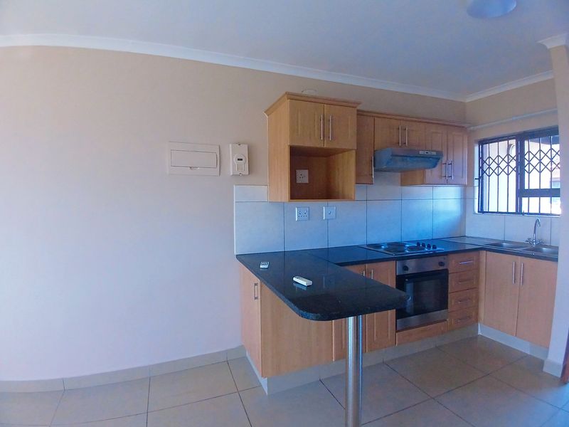 A functional kitchen featuring light wood cabinetry, granite countertops, built-in oven and hob, and tiled flooring, offering a clean and practical workspace.