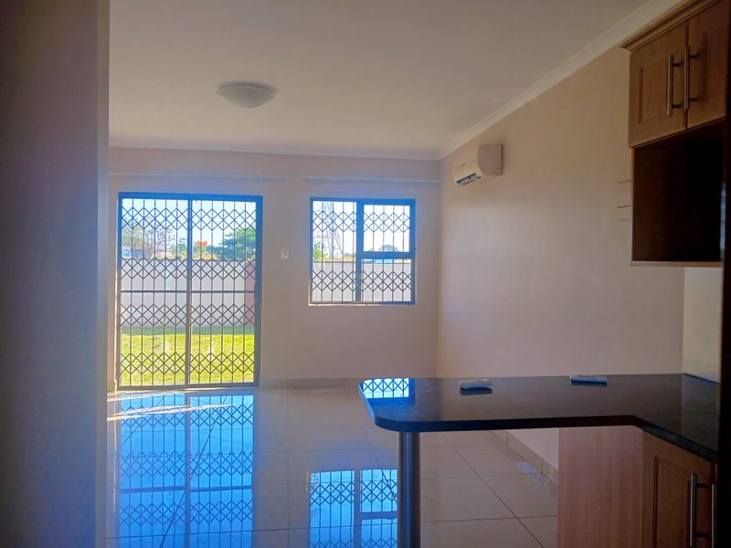 Bright open-plan living area featuring tiled floors, a breakfast bar, and direct access to the garden through secure sliding doors.