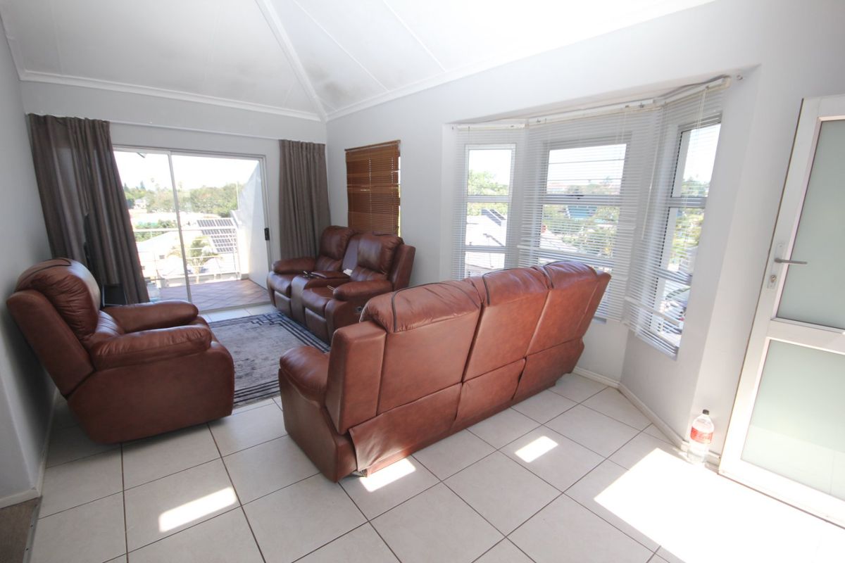 A bright living room featuring tiled flooring, a vaulted ceiling, and a bay window with access to an attached balcony.