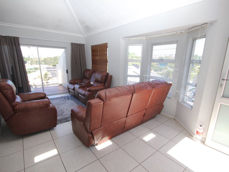 A bright living room featuring tiled flooring, a vaulted ceiling, and a bay window with access to an attached balcony.