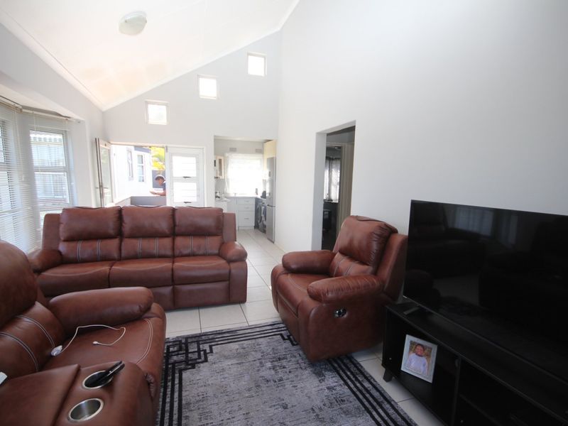 Spacious open-plan living area featuring a high vaulted ceiling, tiled flooring, and natural light from clerestory windows, with direct access to an outdoor space.