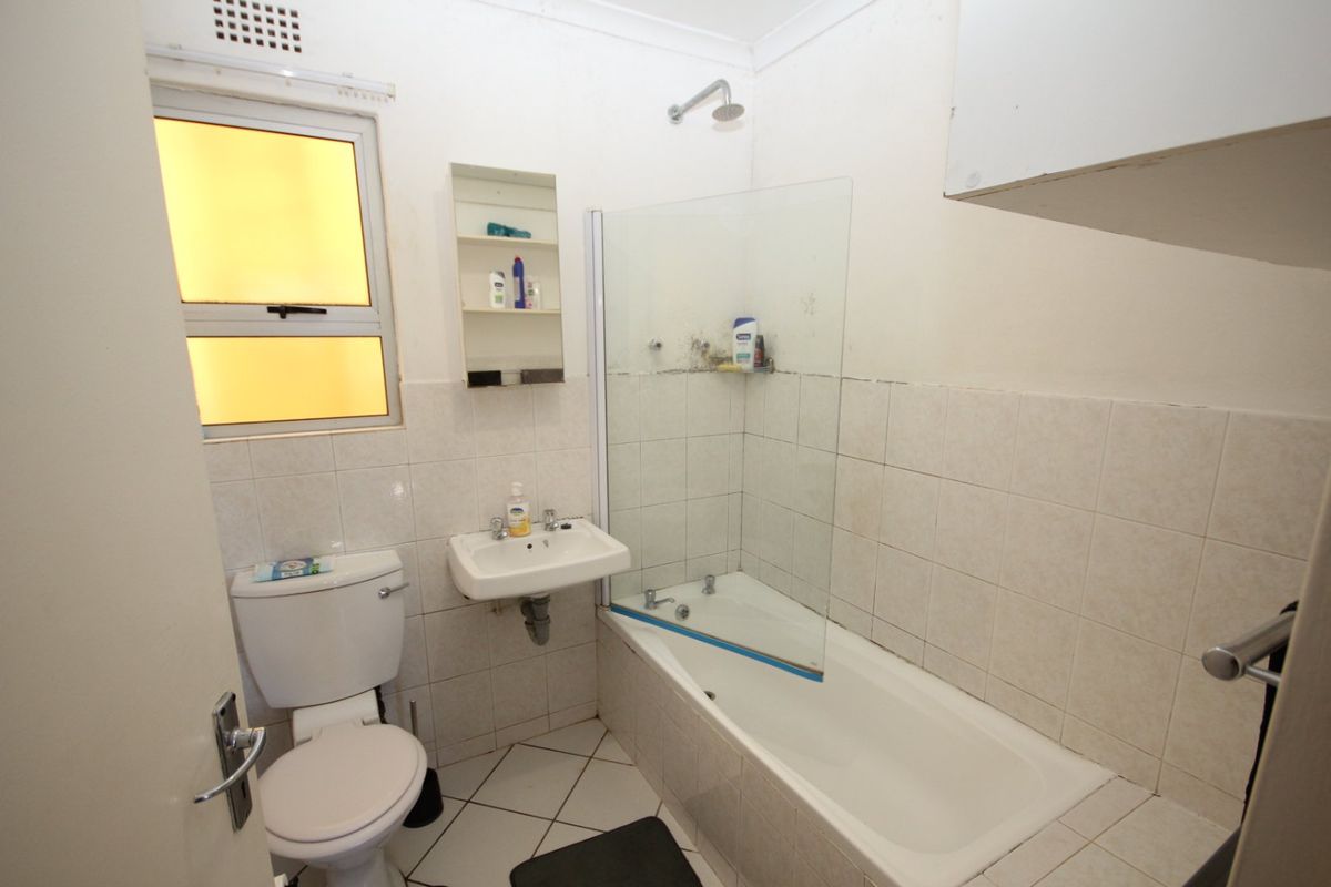 A functional bathroom featuring a bathtub with a glass shower screen, wall-mounted basin, and toilet, finished with tiled flooring and wall splashbacks.