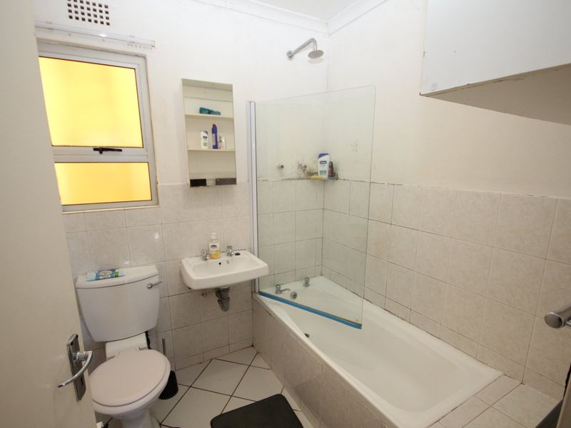 A functional bathroom featuring a bathtub with a glass shower screen, wall-mounted basin, and toilet, finished with tiled flooring and wall splashbacks.
