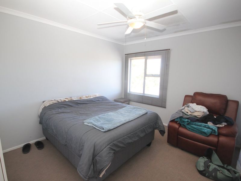 A bedroom featuring a ceiling fan, venetian blinds, and built-in storage, with visible water staining on the ceiling requiring attention.