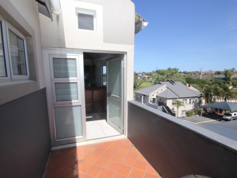 A private balcony featuring terracotta tiling, a sliding glass door entrance, and a solid balustrade with views over the surrounding residential complex.