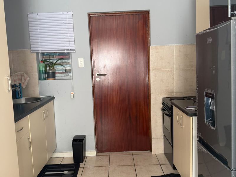 A compact kitchen featuring tiled flooring, built-in cabinetry, a stainless steel sink, and a freestanding stove, requiring some cosmetic updates to the wall finishes.