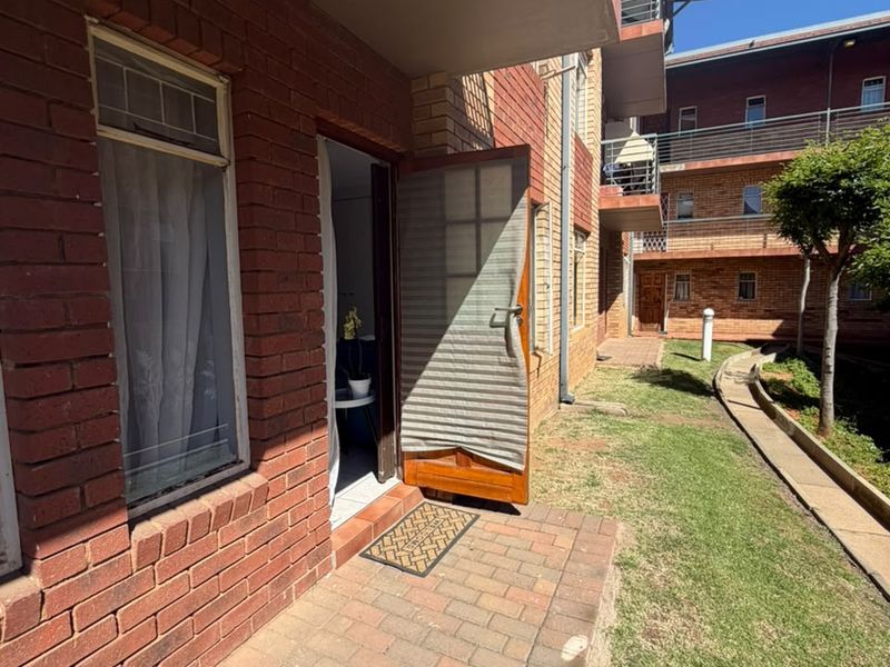A ground-level brick paved patio area featuring an exposed brick facade and a security screen door leading into the apartment.