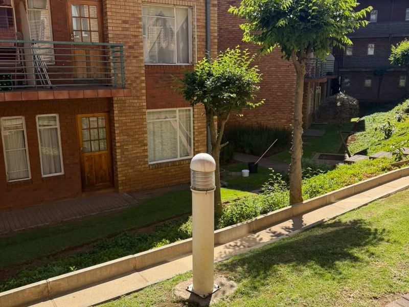A view of the apartment complex rear exterior featuring brick facade, private balconies with metal railings, and a landscaped garden area with paved pathways.