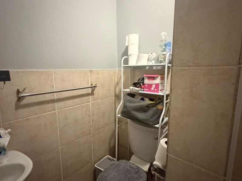 A compact bathroom featuring tiled walls and flooring, a pedestal basin, and a standard toilet with an integrated towel rail.